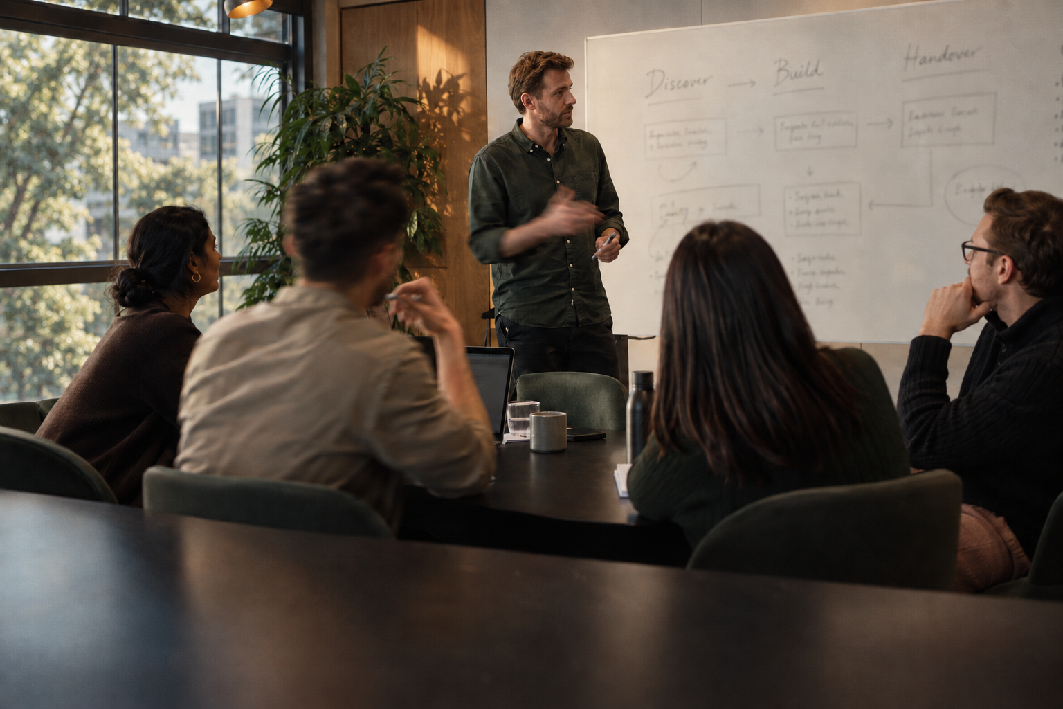 Workshop with a presenter at a softly focused whiteboard and a group of young professionals.
